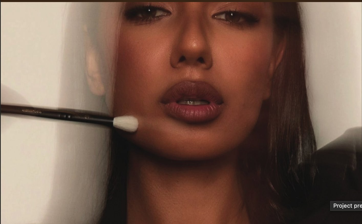 Editorial portrait — warm-toned beauty close-up, soft brush against the cheek and lips.