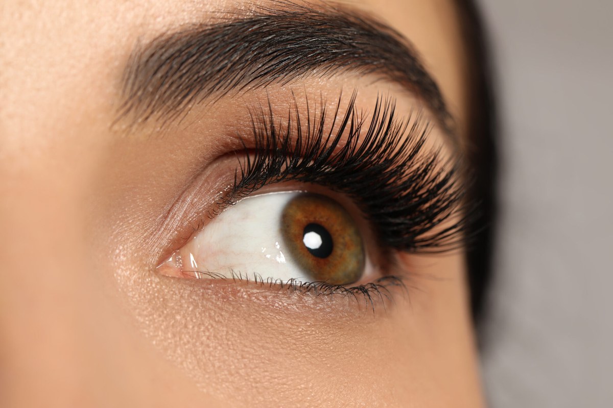 Macro close-up of long, lifted natural eyelashes with a soft brow above.